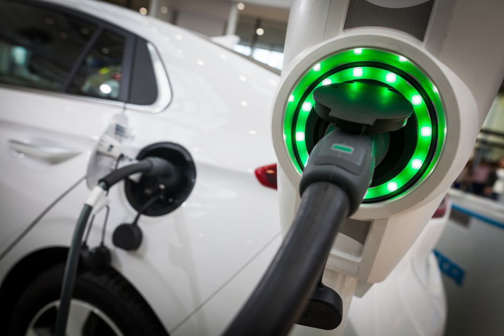 A White Electric Car Is Being Charged at A Charging Station — All Star Electrical Services in Figtree, NSW