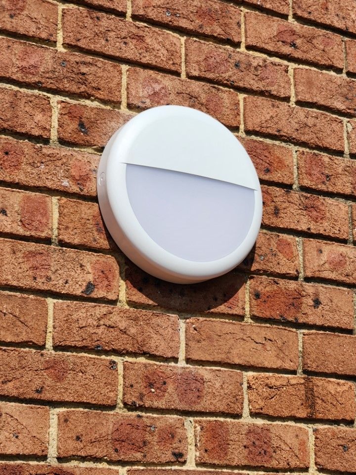 White circular outdoor light fixture mounted on a red brick wall.