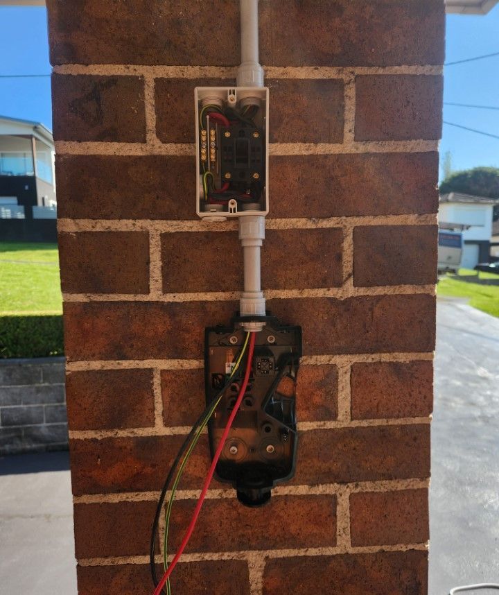 Electrical wiring components mounted on a brick pillar. Exposed wires, conduit, and junction box.