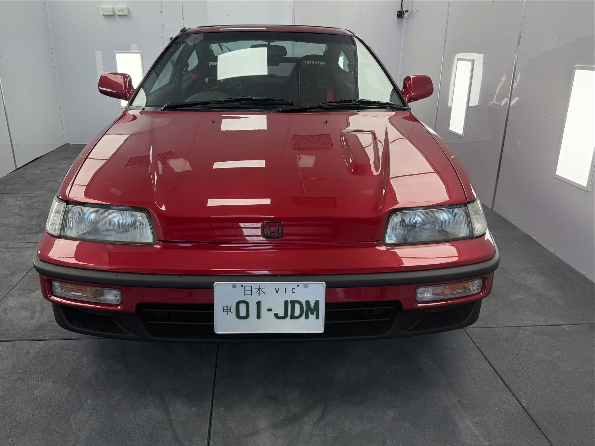 Red Honda CRX front view, Japanese license plate, parked indoors.