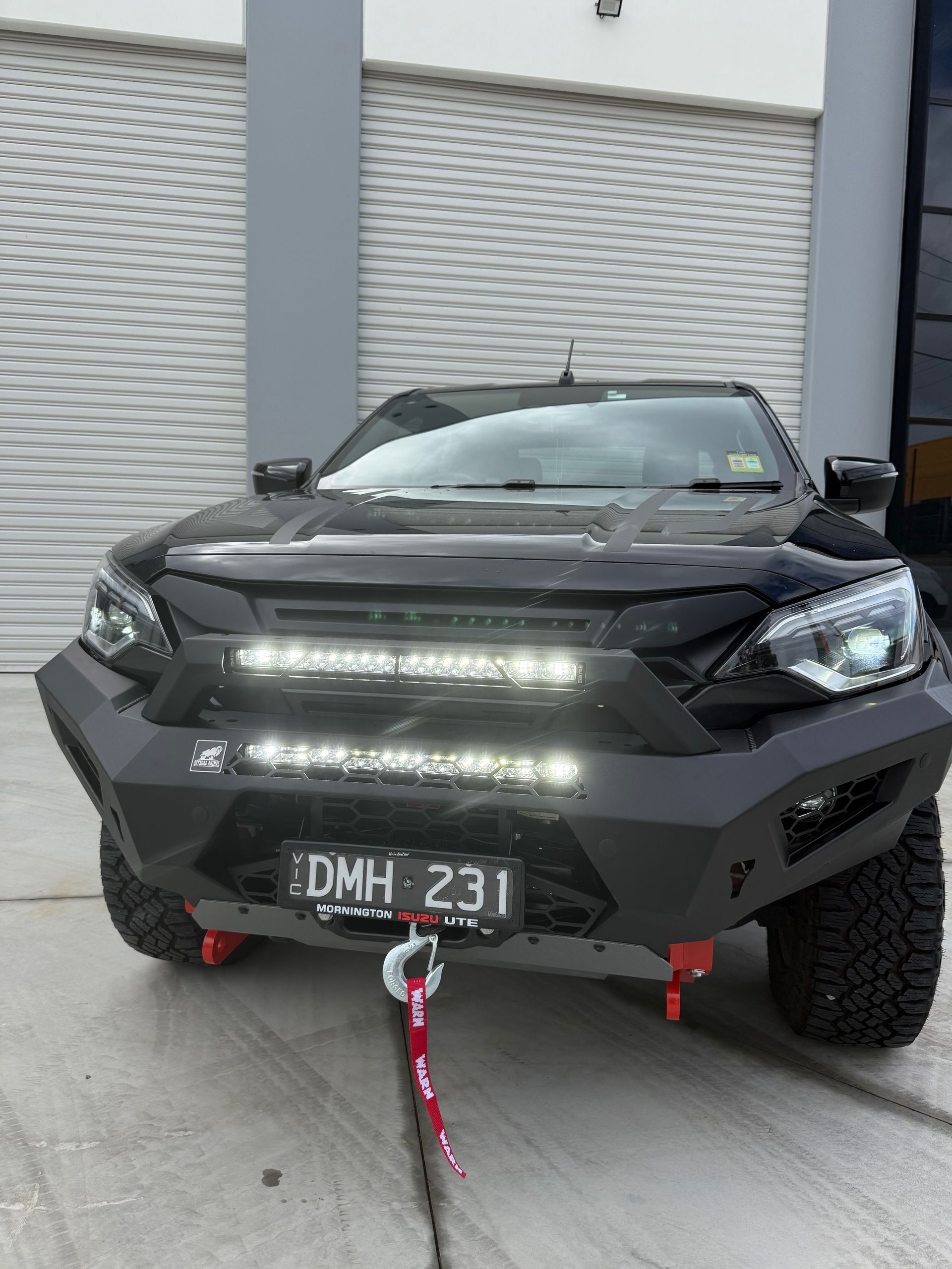 Black pickup truck with modified front bumper, tow hooks, and LED lights, parked outdoors.