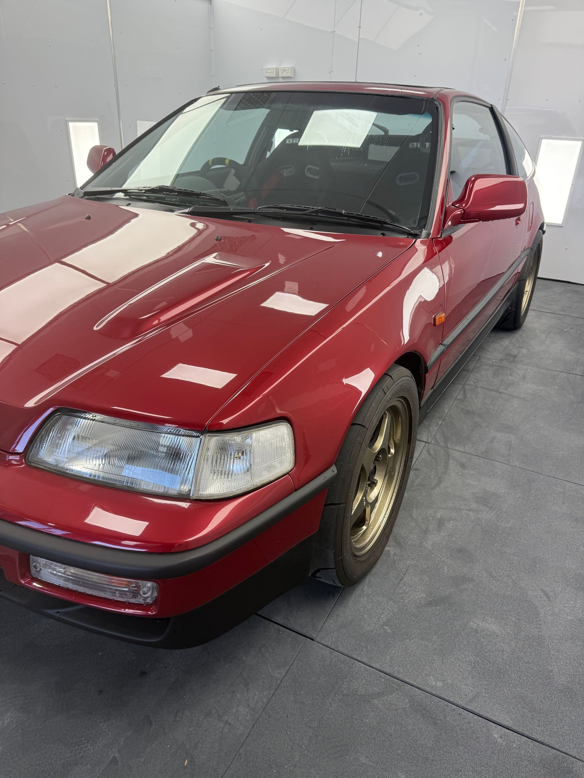 Red Honda CRX coupe, gold wheels, parked in a studio.