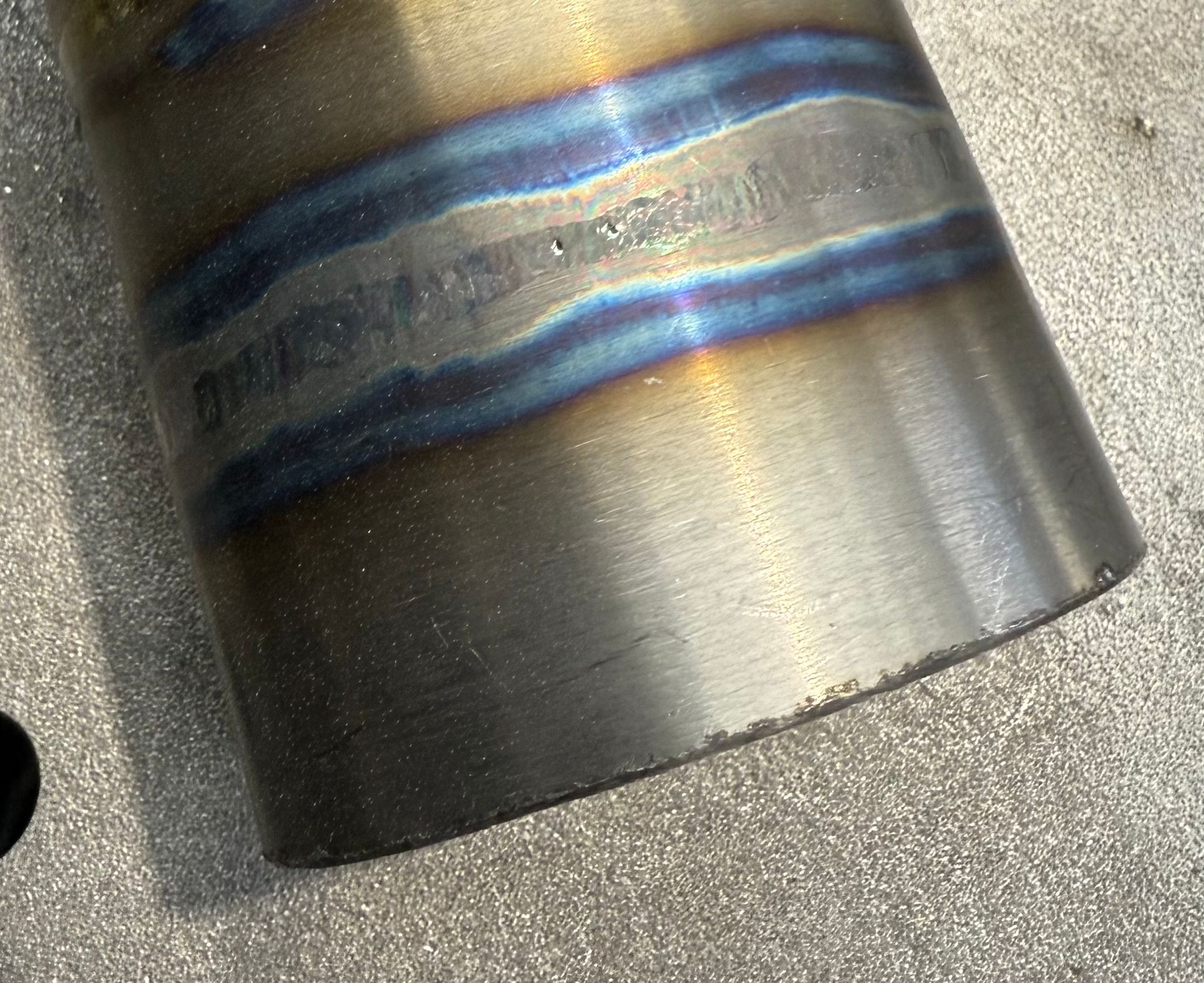 Metal pipe section with a welded seam, exhibiting blue and gold heat discoloration.