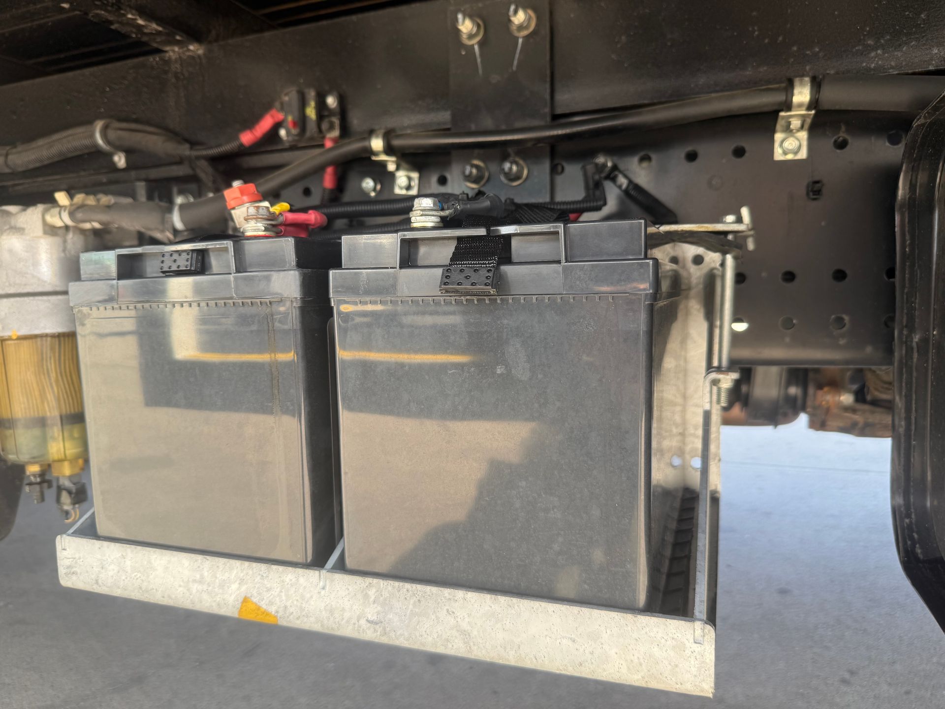 Two large black batteries in a metal tray under a vehicle chassis.