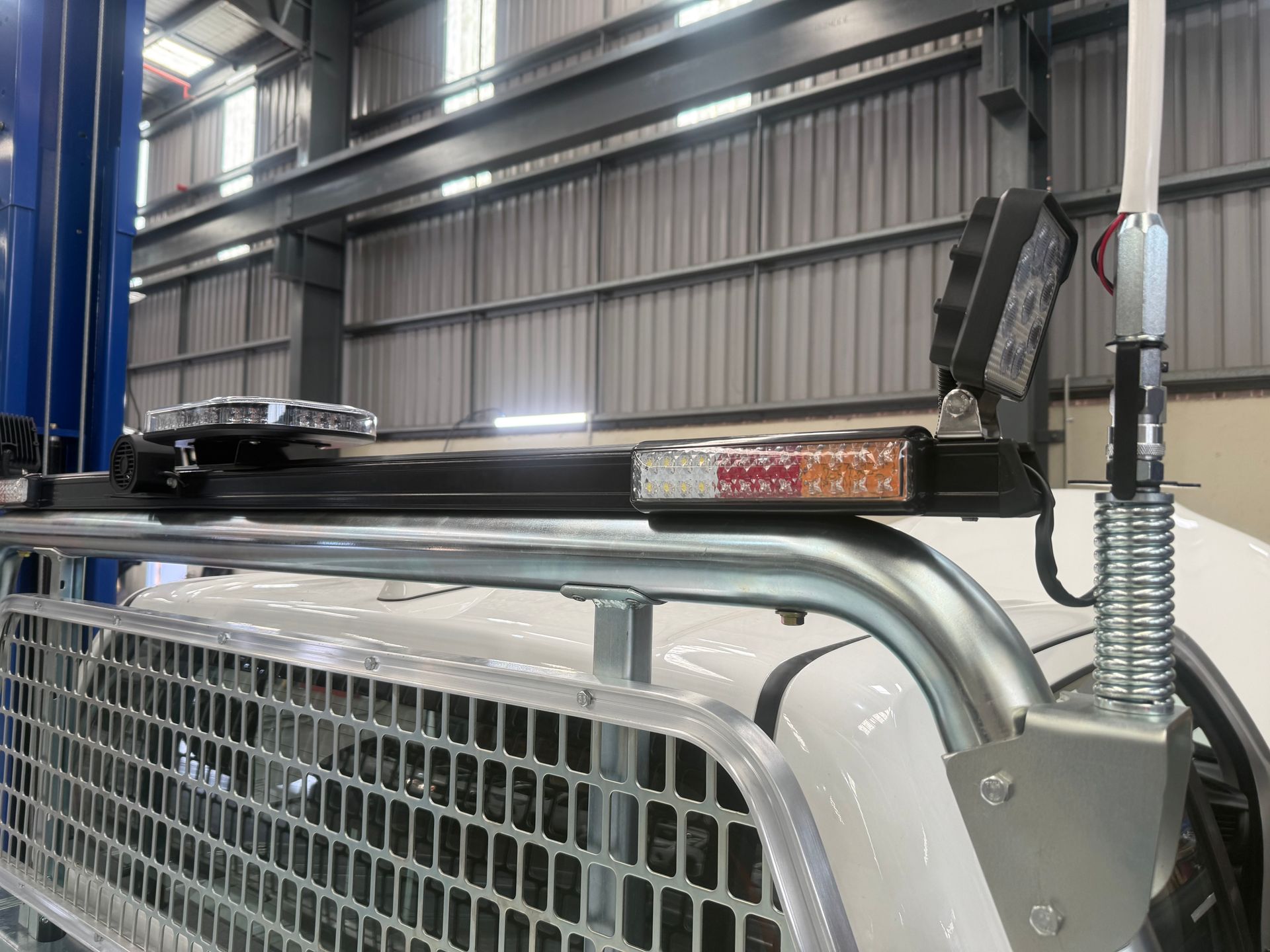 A light bar mounted on a white truck's roll cage, with amber and white lights, and an antenna.