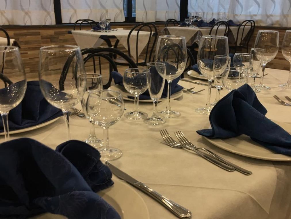 Un tavolo da ristorante apparecchiato con tovaglie bianche, tovaglioli blu, bicchieri da vino e posate.