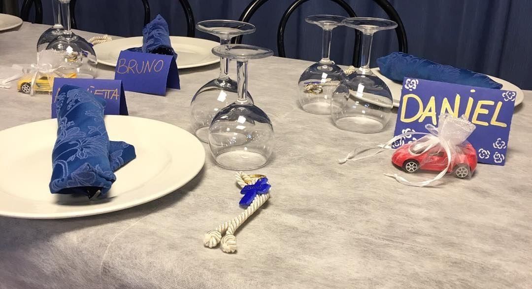 Una tavola apparecchiata con tovaglioli blu, bicchieri da vino e segnaposto blu, uno dei quali reca la scritta