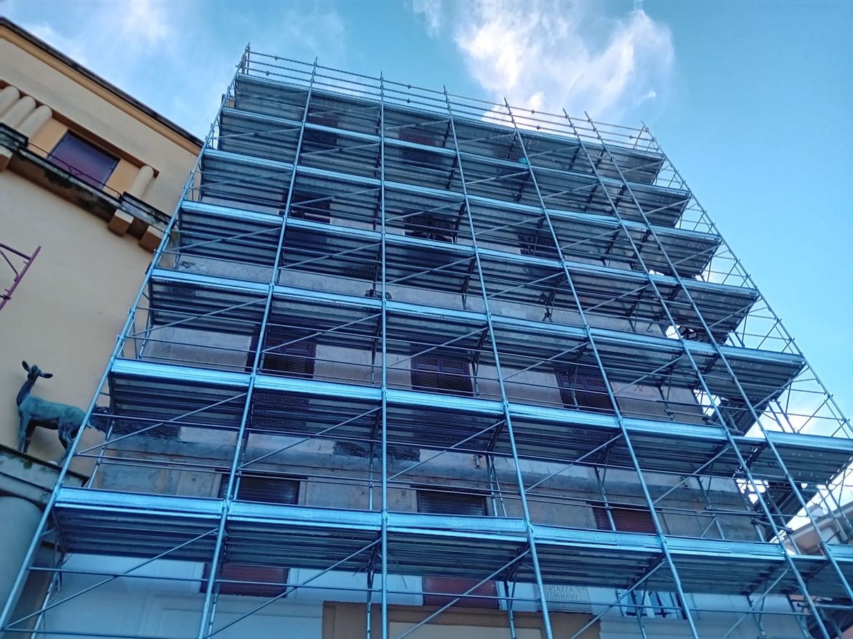 Ponteggi blu sulla facciata di un edificio, con un cielo azzurro brillante sullo sfondo