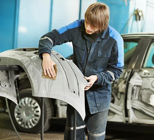 Person examining a detached car panel in an auto repair shop