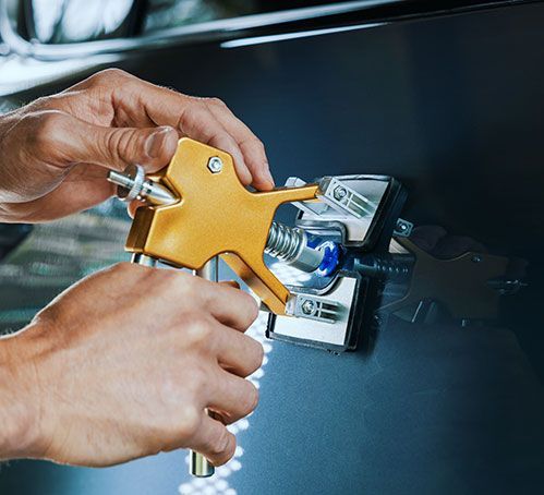 Hands using a gold suction-cup dent puller on a black car door.