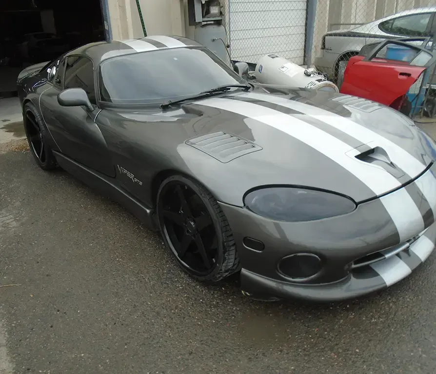 Gray sports car with white racing stripes parked outdoors in a driveway