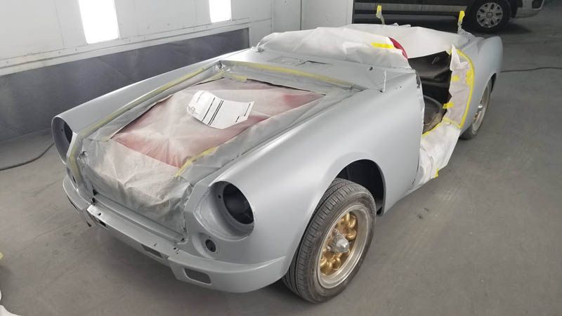 Partially restored silver vintage car body in a garage, covered with masking tape and protective sheets