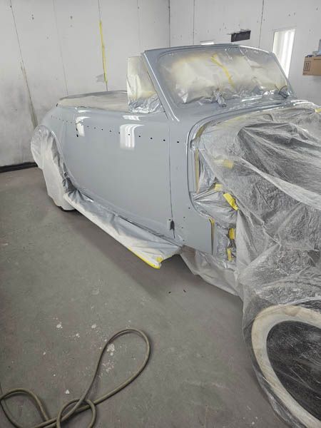 Gray car under plastic and tape in a workshop, in the middle of a repaint or restoration.