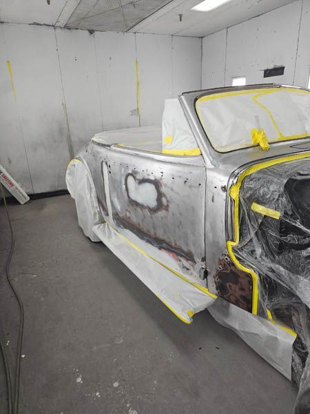 Classic car body prepped and masked with tape in a paint shop booth