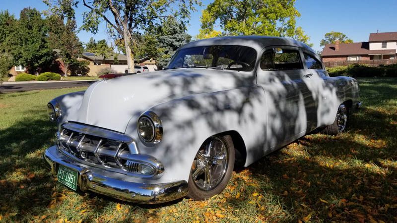 Classic white vintage car parked on grass under trees in a sunny neighborhood yard