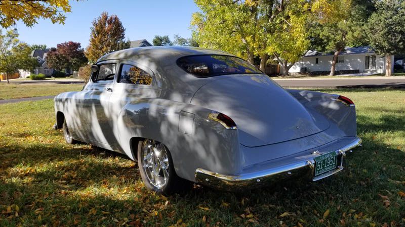 Silver vintage car parked on a grassy lawn with trees and houses in the background