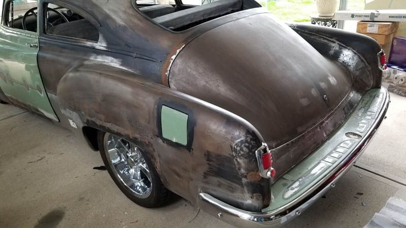 Rusty vintage car in a garage, rear view with faded brown paint and chrome bumper