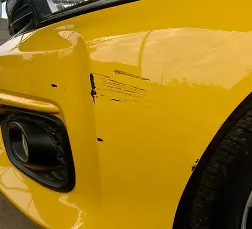 Close-up of a yellow car’s side with black scuff marks and paint scratches near the wheel