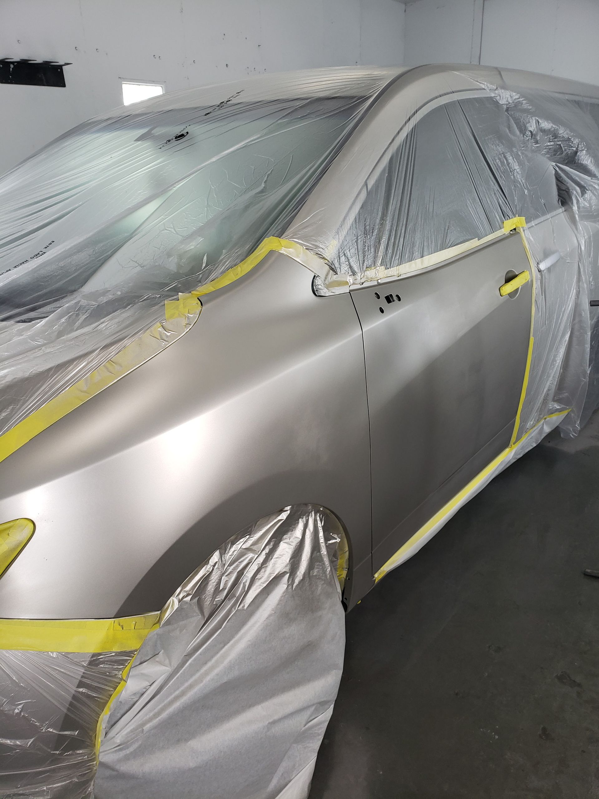 Silver car masked with plastic and yellow tape in a paint booth