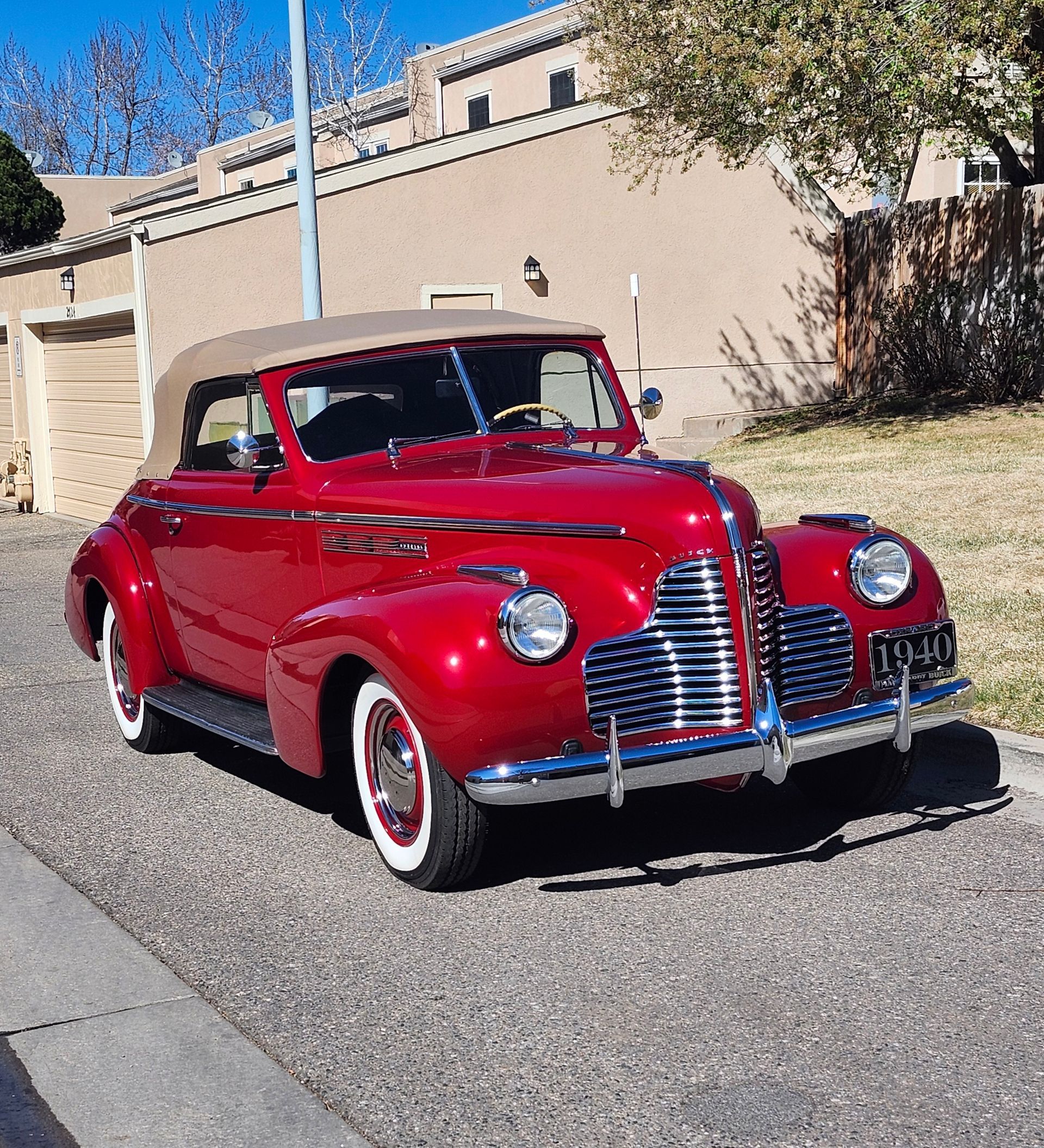 Red vintage convertible parked on a street in front of a beige house.