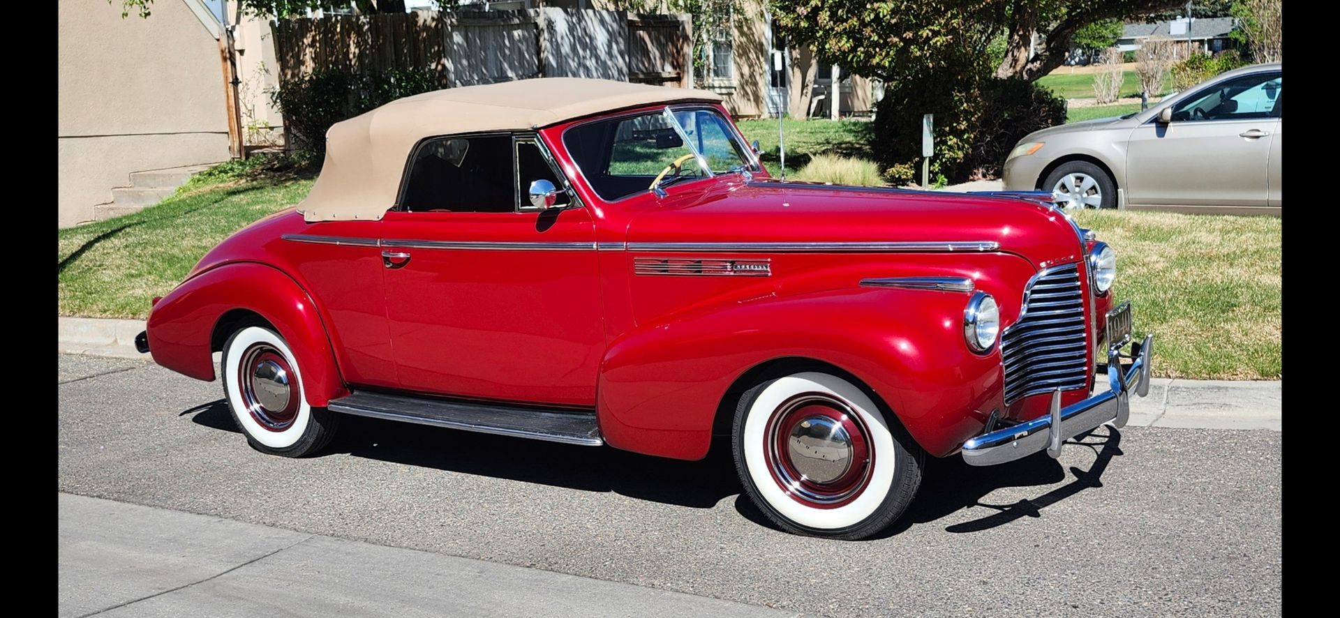 Red vintage convertible car with beige soft top parked on a residential street