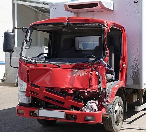 Severely damaged red truck cab after a collision, parked outdoors beside a building.