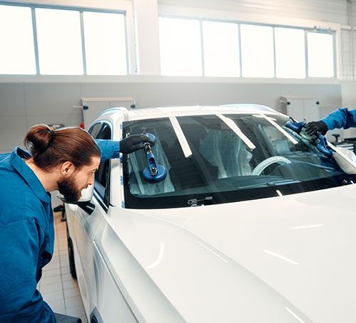 Two workers polishing a white car windshield in a bright auto shop