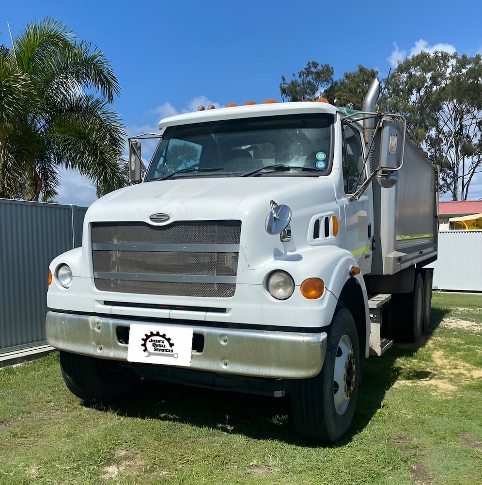 A White Dump Truck Is Parked In A Grassy Field — Josh's Diesel Services in Gladstone, QLD