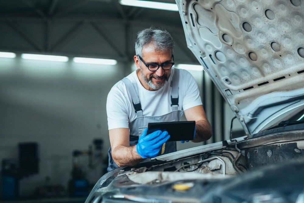 A Man Is Looking At A Tablet While Working On A Car — Josh's Diesel Services in Boyne Island, QLD