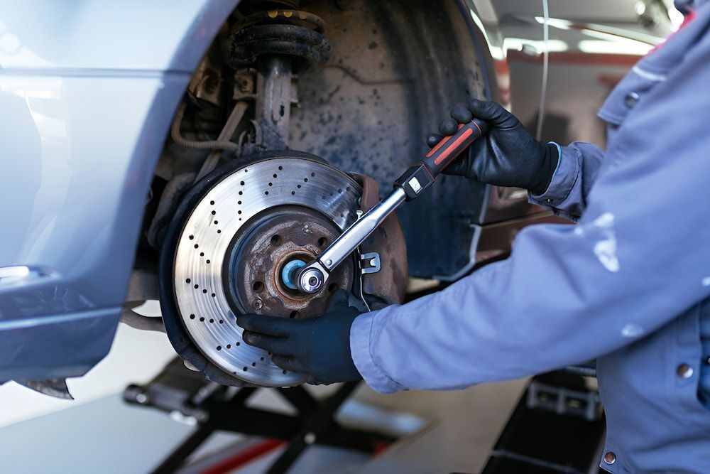 A Man Is Working On The Brake Disc Of A Car With A Wrench — Josh's Diesel Services in Bororen, QLD