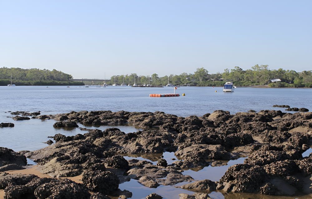 A Body Of Water With Rocks In The Foreground And Boats — Josh's Diesel Services in Boyne Island, QLD