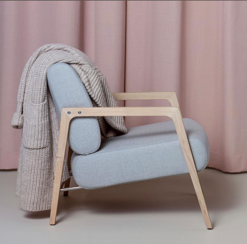 Moderne lichtblauwe stoel met houten frame en beige gebreide plaid tegen roze gordijnen
