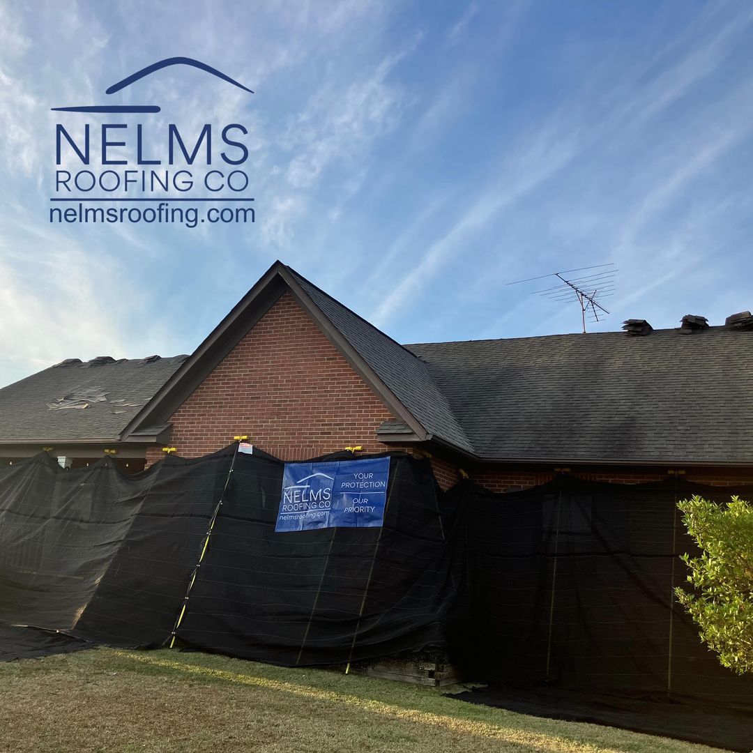 Nelms Roofing banner on house roof during roof repair, with dark tarps and exposed shingles