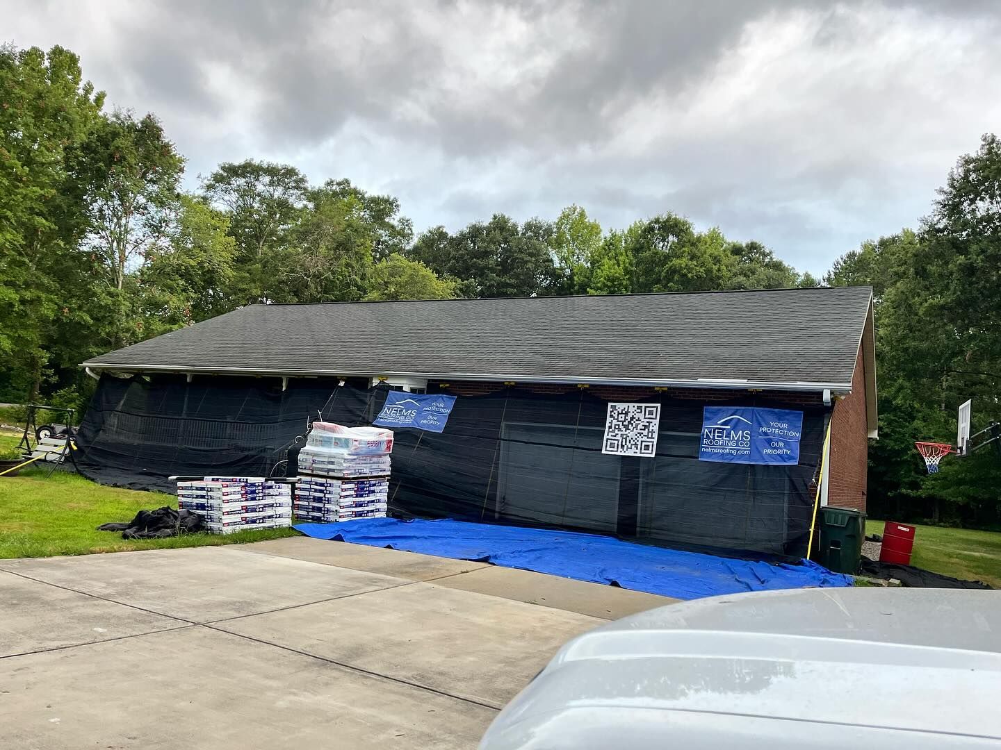 Small dark building with blue tarp and protest-style signs beside a driveway, trees in the background