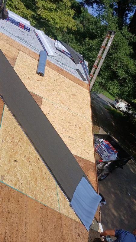 Roof under construction with plywood sheathing, gray underlayment strips, and blue tape on a sloped roof