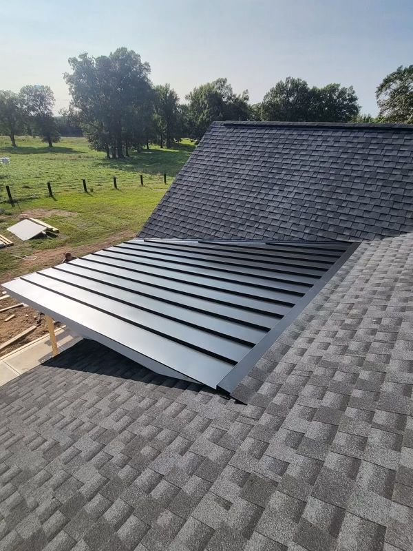 Metal roof on a house with shingle roofing, shown beside a grassy yard and trees.