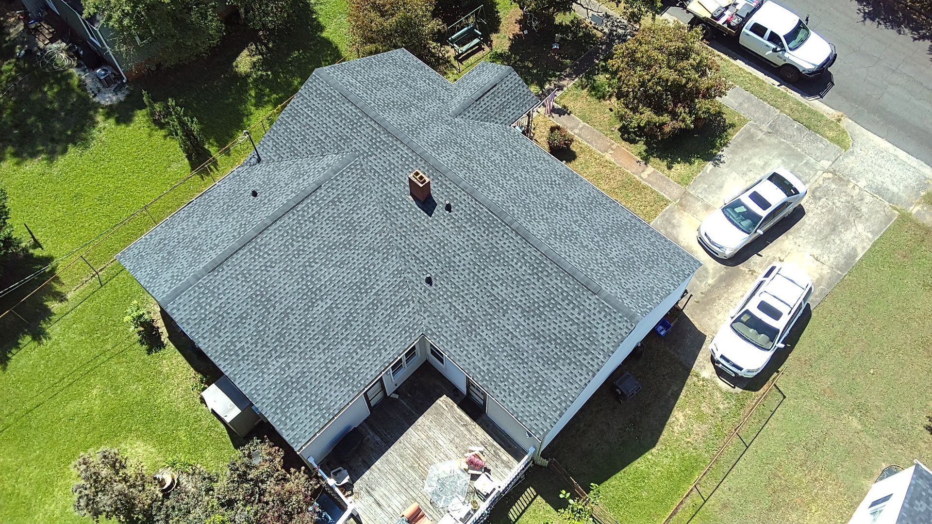 Aerial view of a gray-roofed house with a driveway, lawn, and several parked cars.