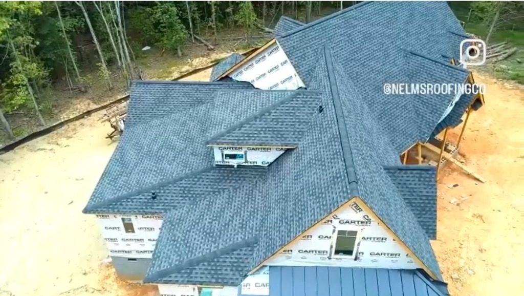 Aerial view of a house with a blue roof surrounded by dirt and trees
