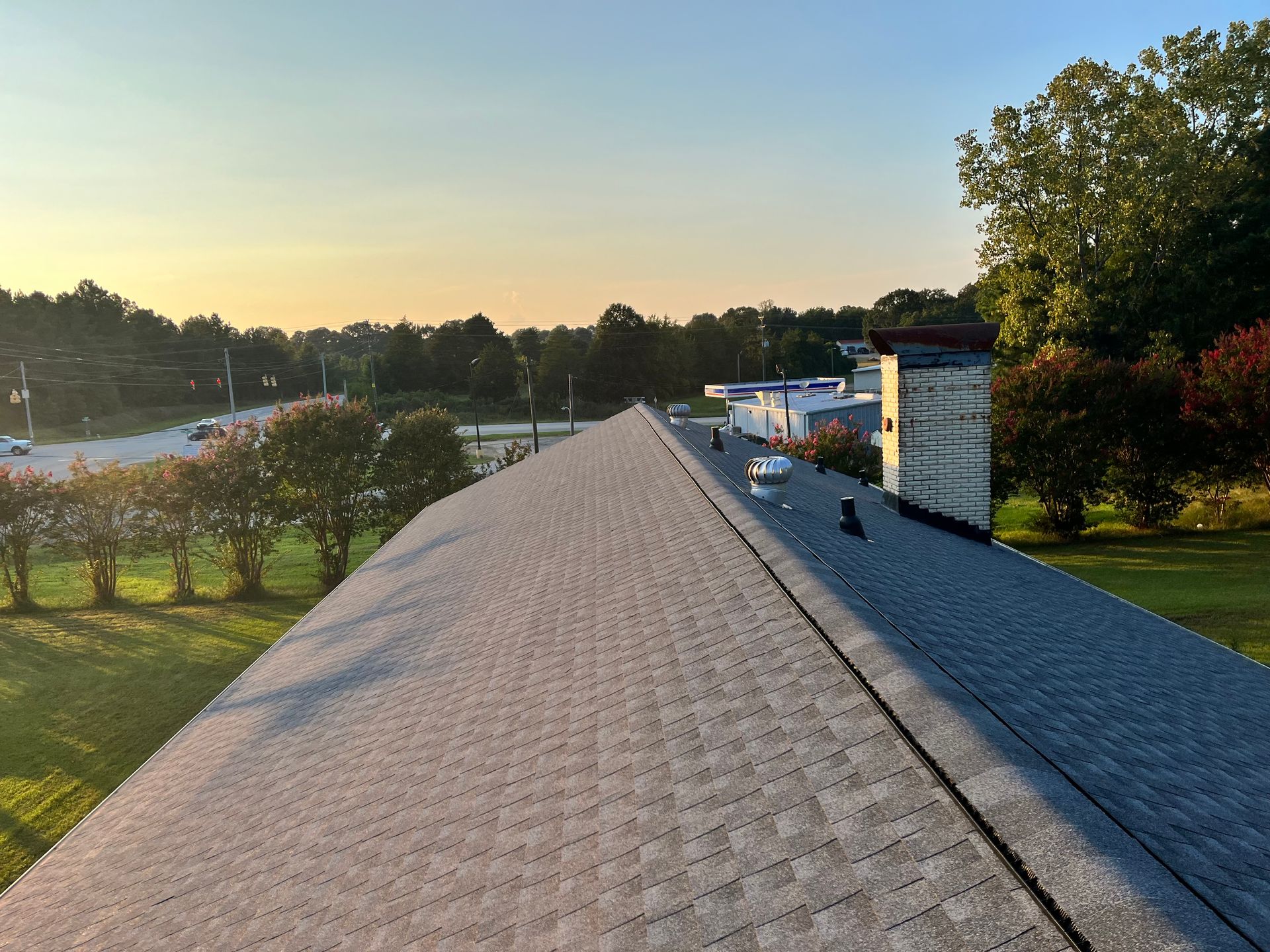 Roofline view at sunset over a neighborhood, with trees and parked cars in the distance