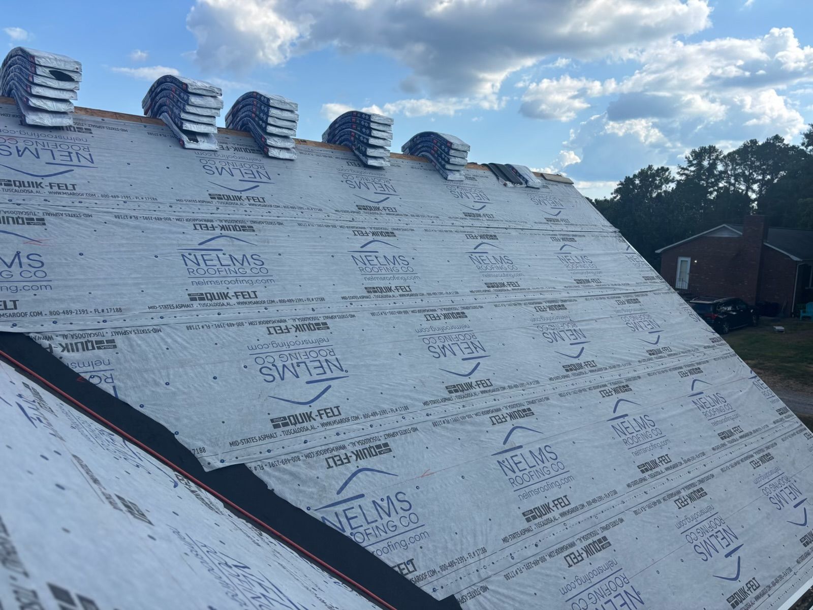 Partially shingled roof with ventilation caps and underlayment under a cloudy sky