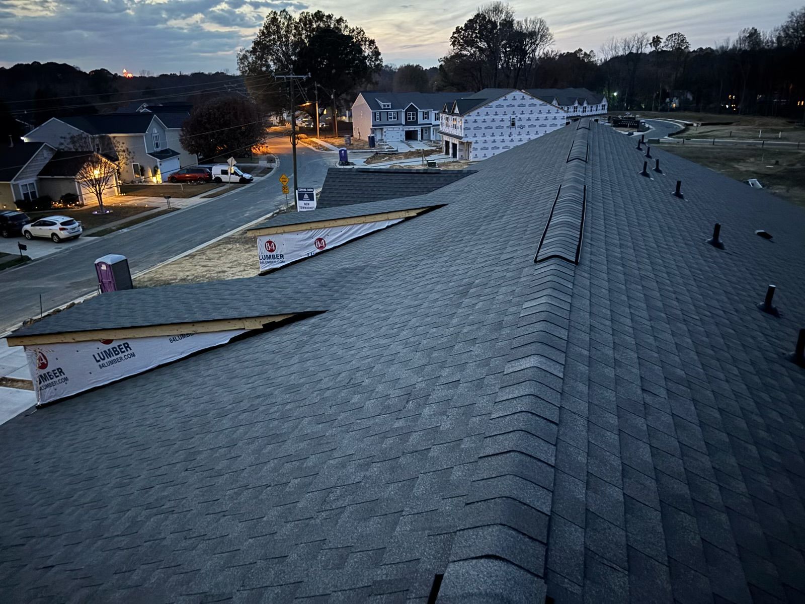 Rooftop at dusk overlooking a suburban neighborhood with houses and streetlights below
