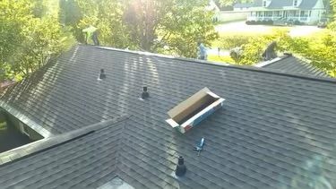 Roof with a skylight under repair, seen from above, surrounded by trees and nearby houses
