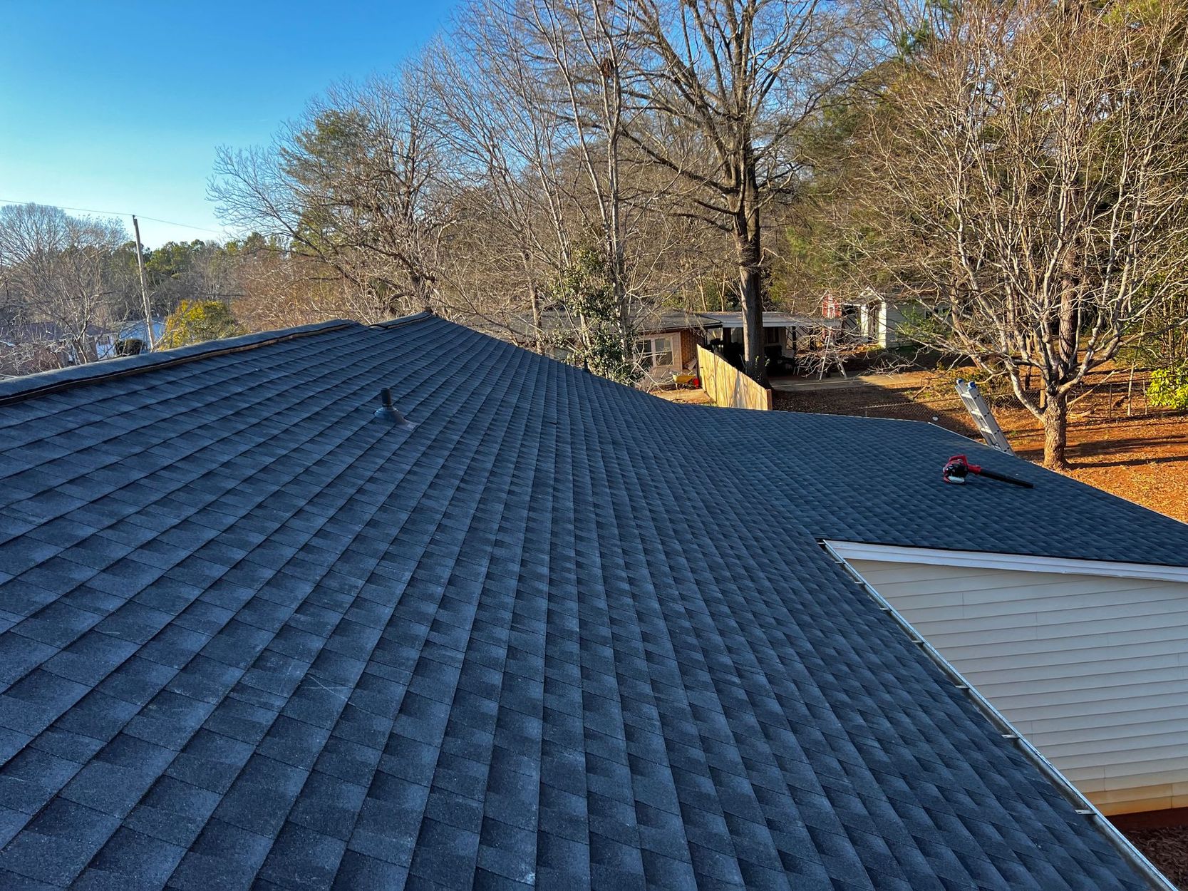 Dark blue shingle roof with trees and neighboring houses in the background