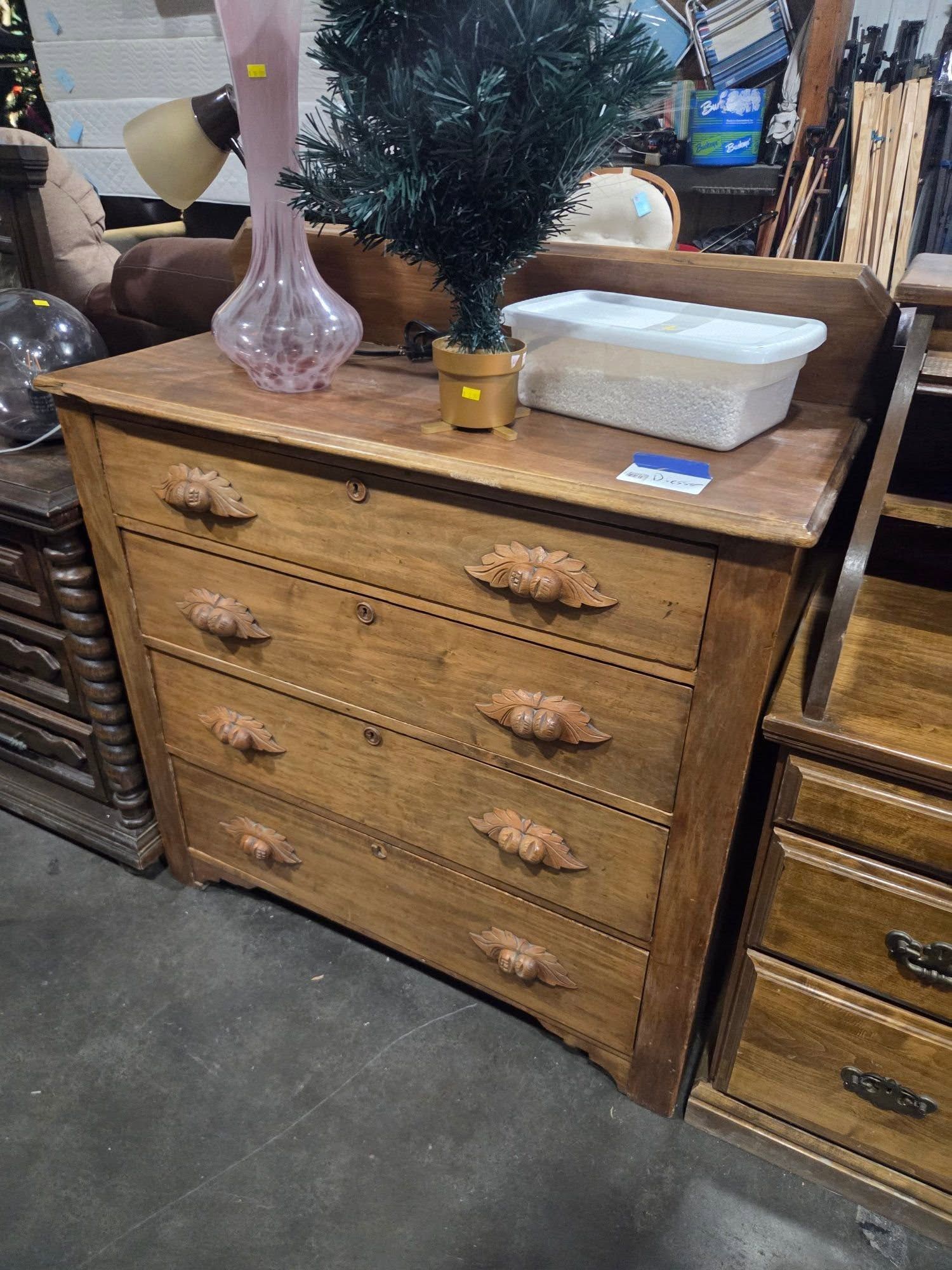 Wooden dresser with four drawers, decorative vases, small artificial tree, and tray in a furniture store