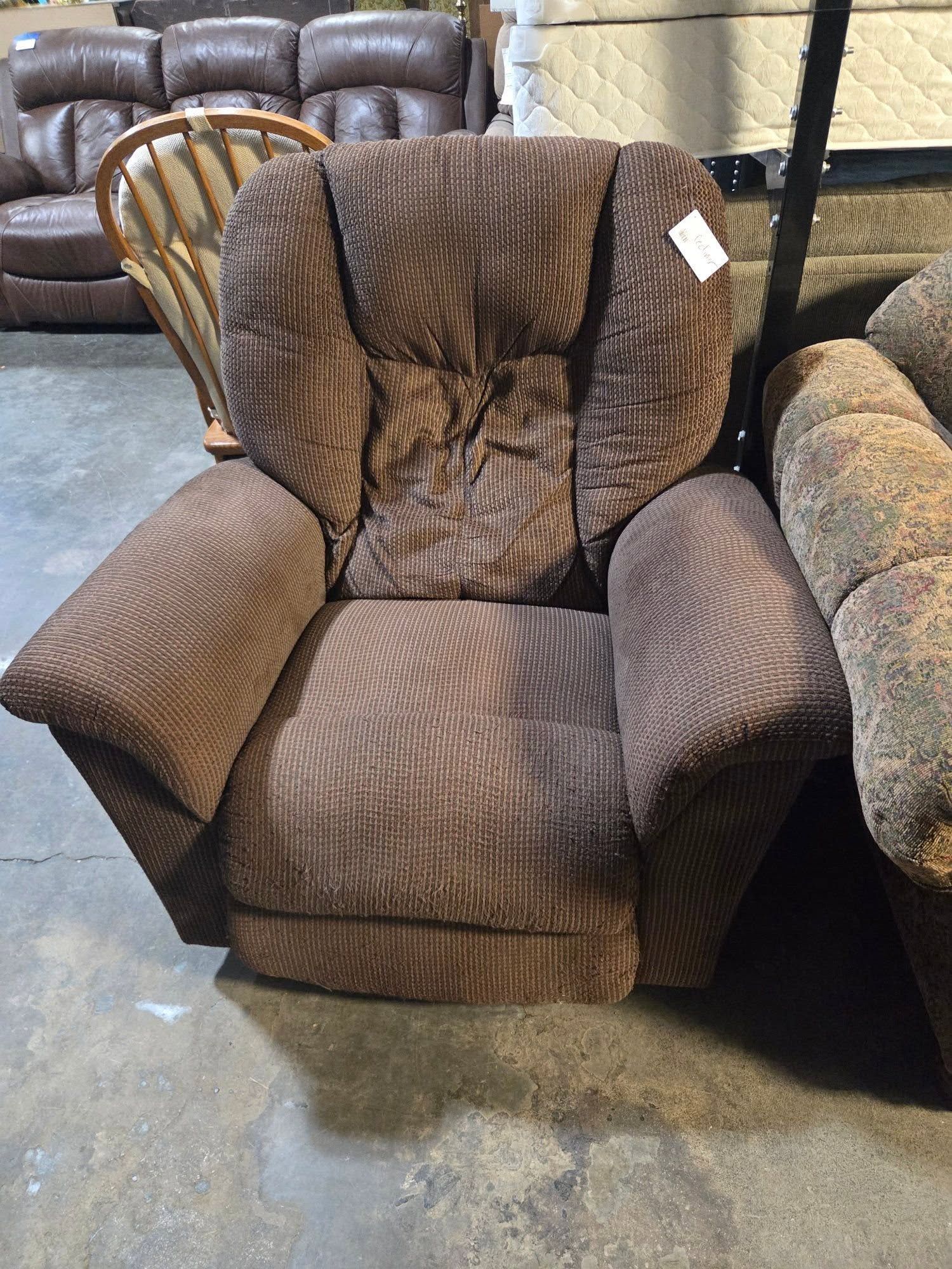 Brown recliner chair with wide armrests and a high back in a furniture store showroom