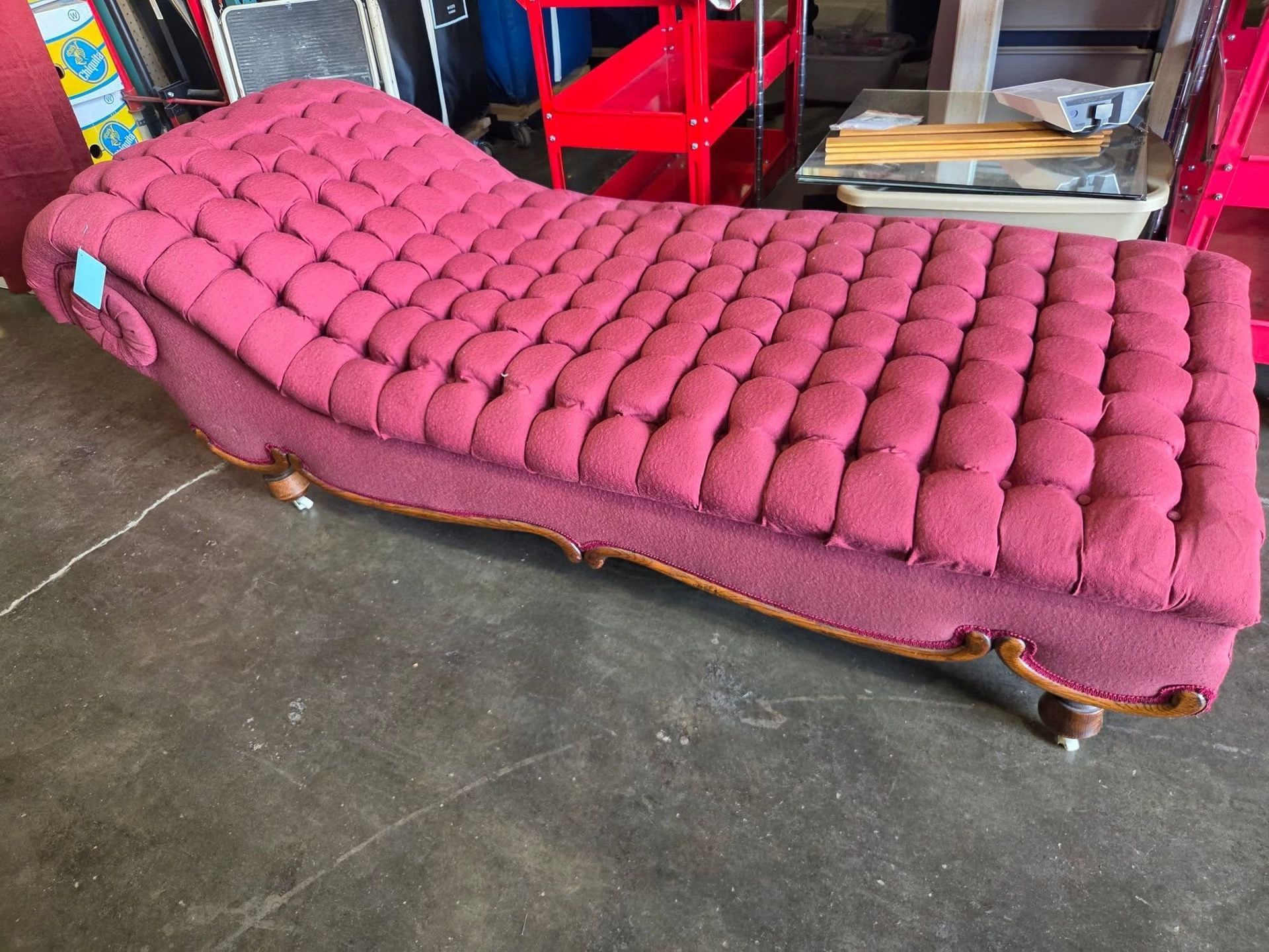Pink tufted chaise lounge in a workshop, with curved wooden legs on a concrete floor.