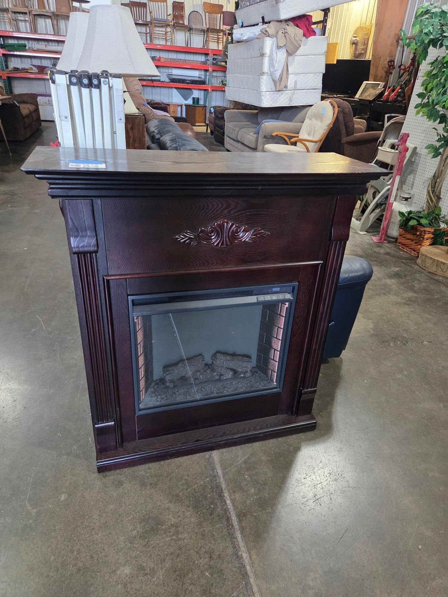 Dark wood electric fireplace mantel in a store aisle, with white wrapped items on top.