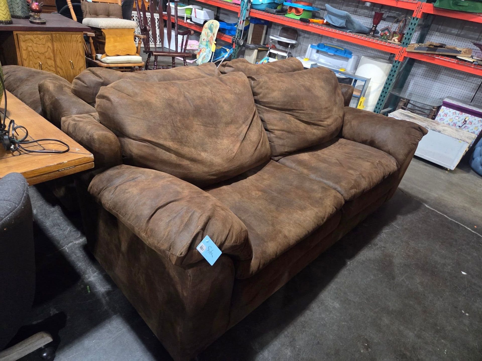 Brown plush loveseat in a retail store aisle, with shelves and furniture visible in the background.