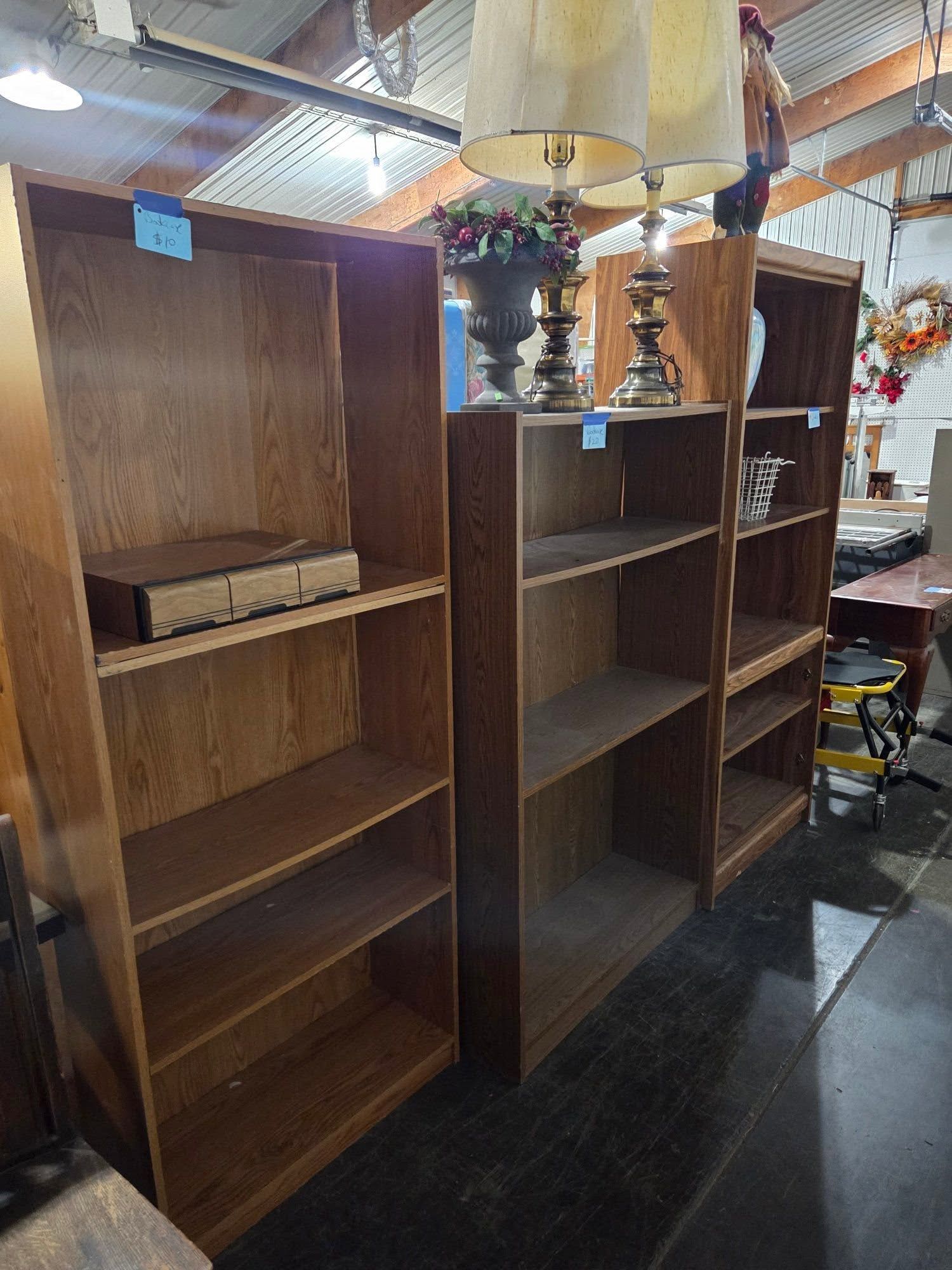 Wooden bookshelves displayed in a store or warehouse aisle under hanging lamps.