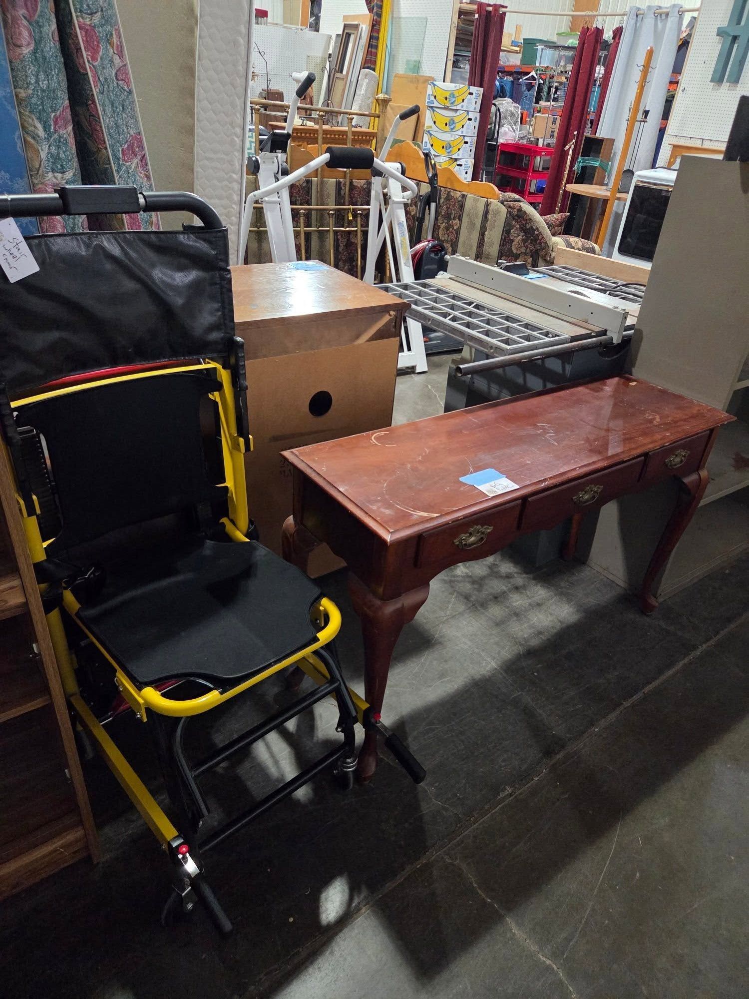 Indoor thrift store aisle with a folded stroller, wooden bench, and boxes among shelves and carts
